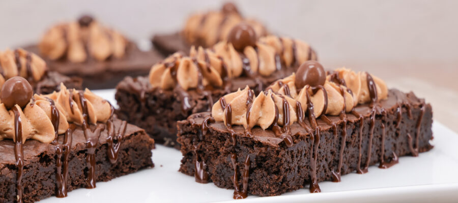 Chocolate brownies topped with swirls of peanut butter frosting and drizzled with chocolate sauce on a white plate.