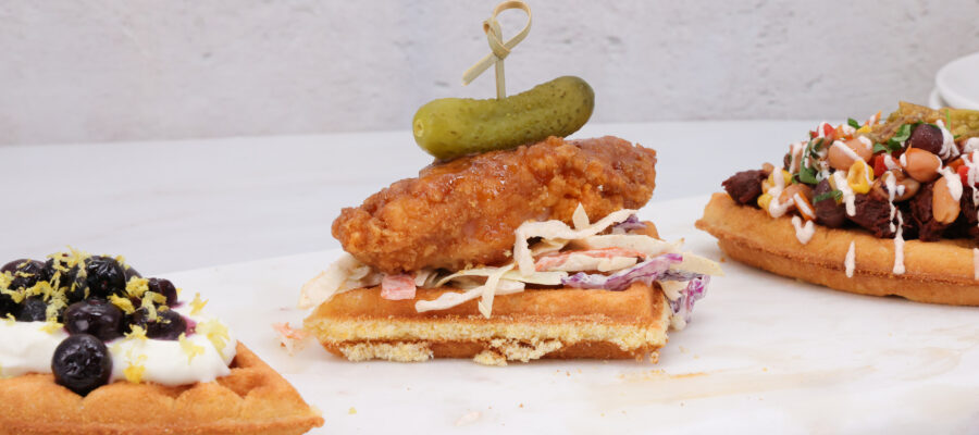 Fried chicken slider on toasted bread with coleslaw and a pickle spear, on a white surface; another loaded toast is nearby.